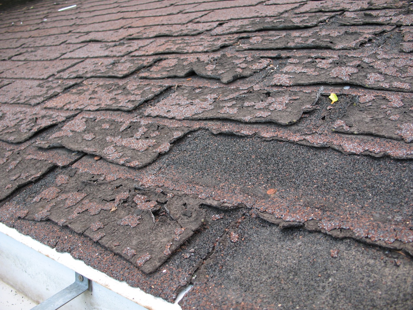 Close-up drone image of failed asphalt shingles exposing the roof deck
